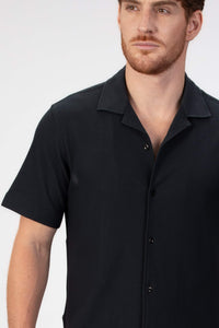 Man wearing a black short-sleeve camp collar shirt on a plain background