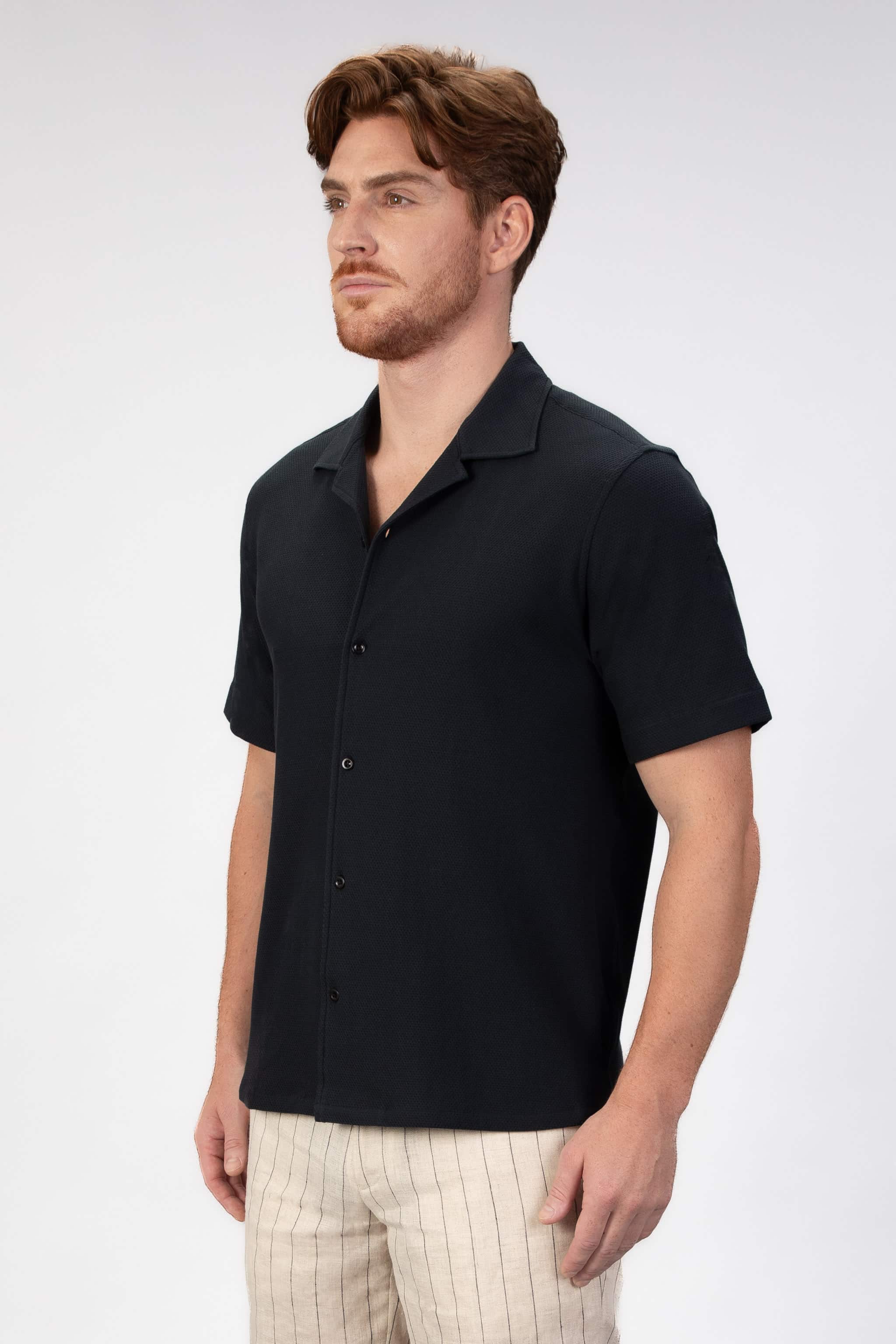 Man wearing a black short-sleeve shirt with buttons on a light gray background