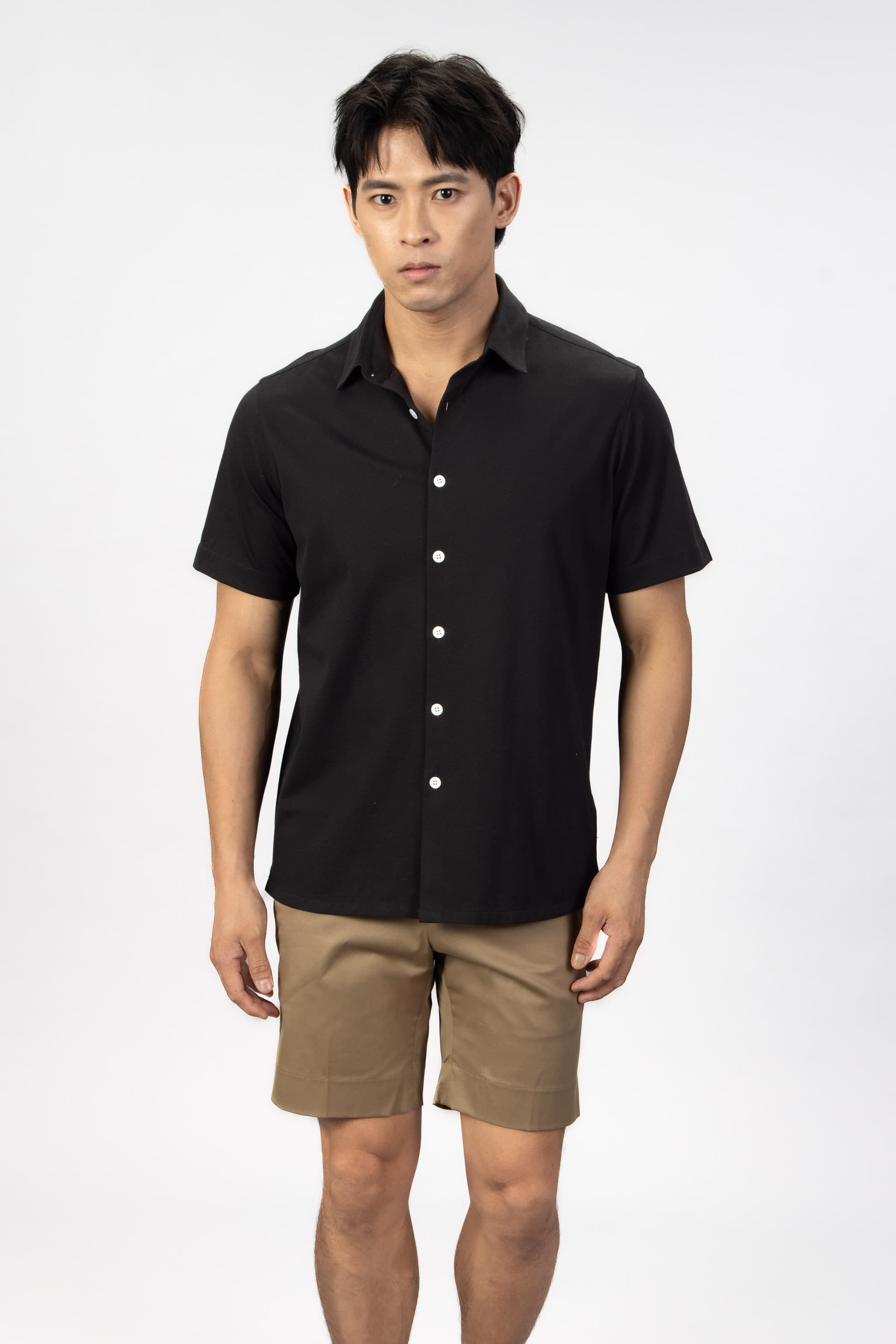 Man wearing a black piquet short sleeve shirt with beige cotton stretch shorts. 