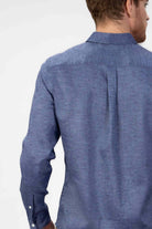 Man wearing a blue button-down shirt  in linen on a light gray background