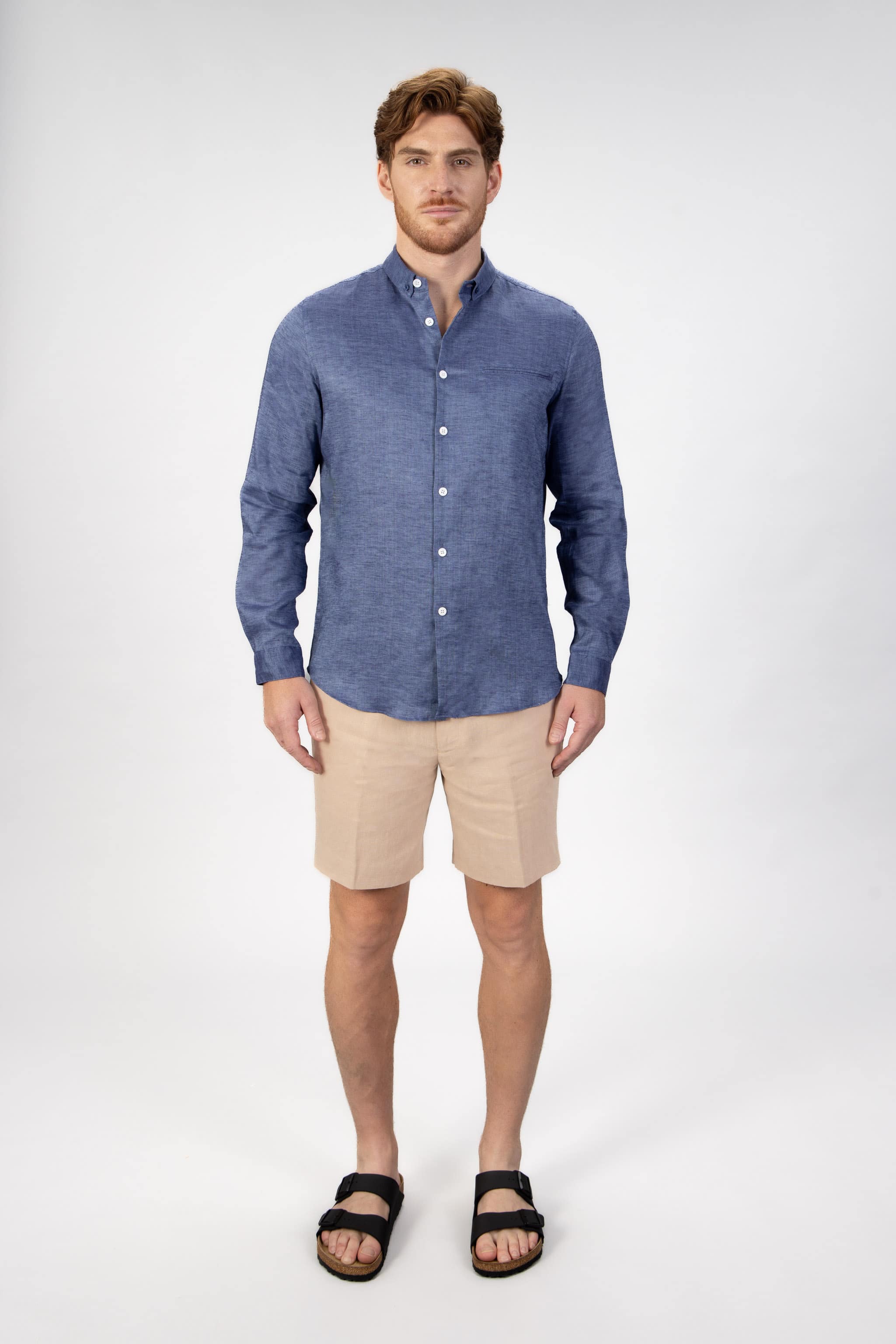 Man wearing a blue button-down shirt  in linen with linen shorts in beige on a light gray background