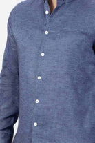 Man wearing a blue button-down shirt  in linen on a light gray background
