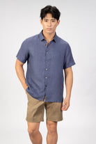 man wearing a blue linen short sleeve shirt with beige cotton shorts on light gray background