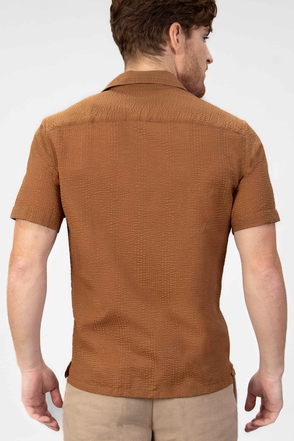 Man wearing a brown seersucker shirt  on a light gray background