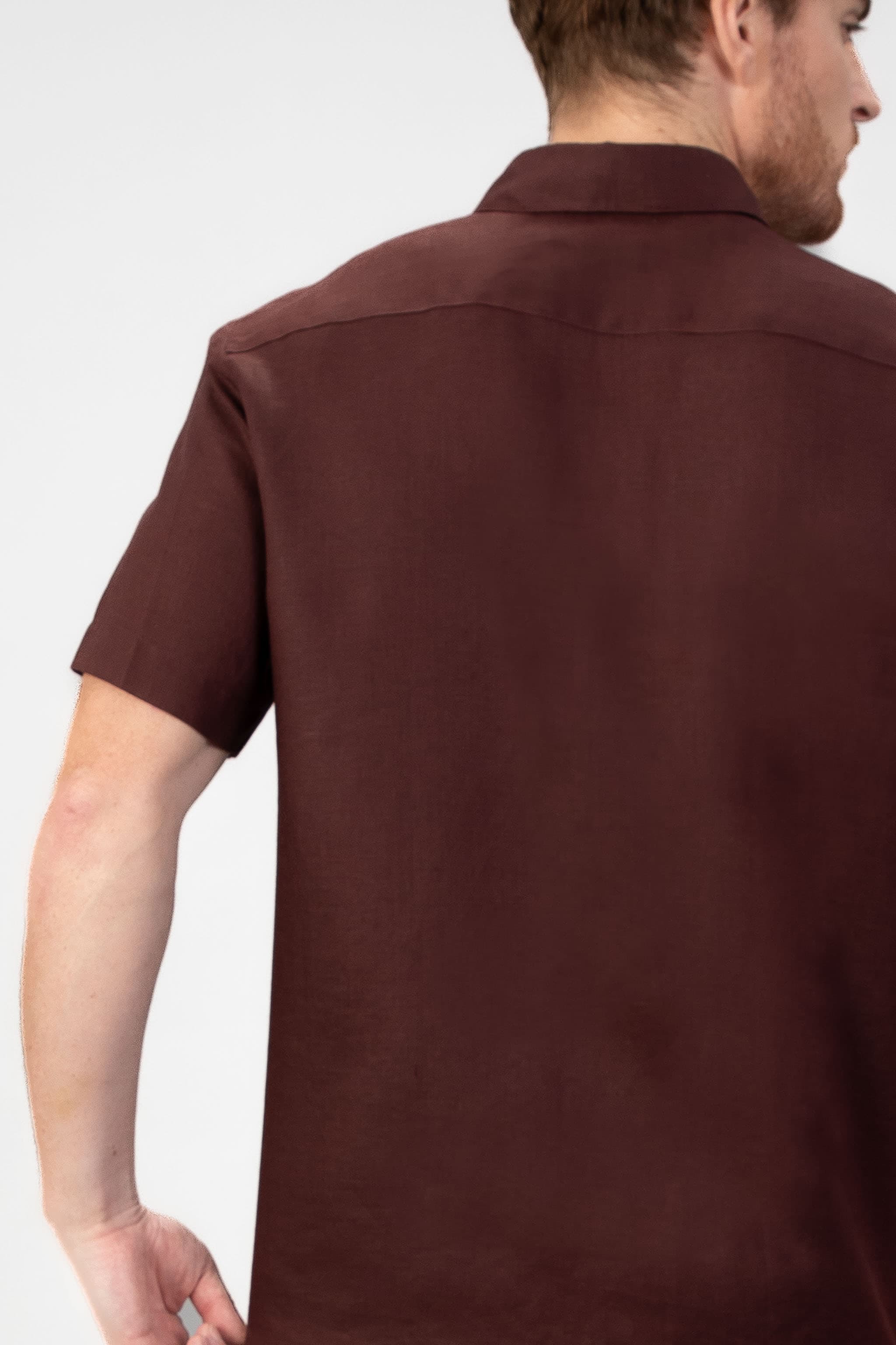 Man wearing a burgundy red short sleeve linen shirt with beige striped linen shorts on light gray background