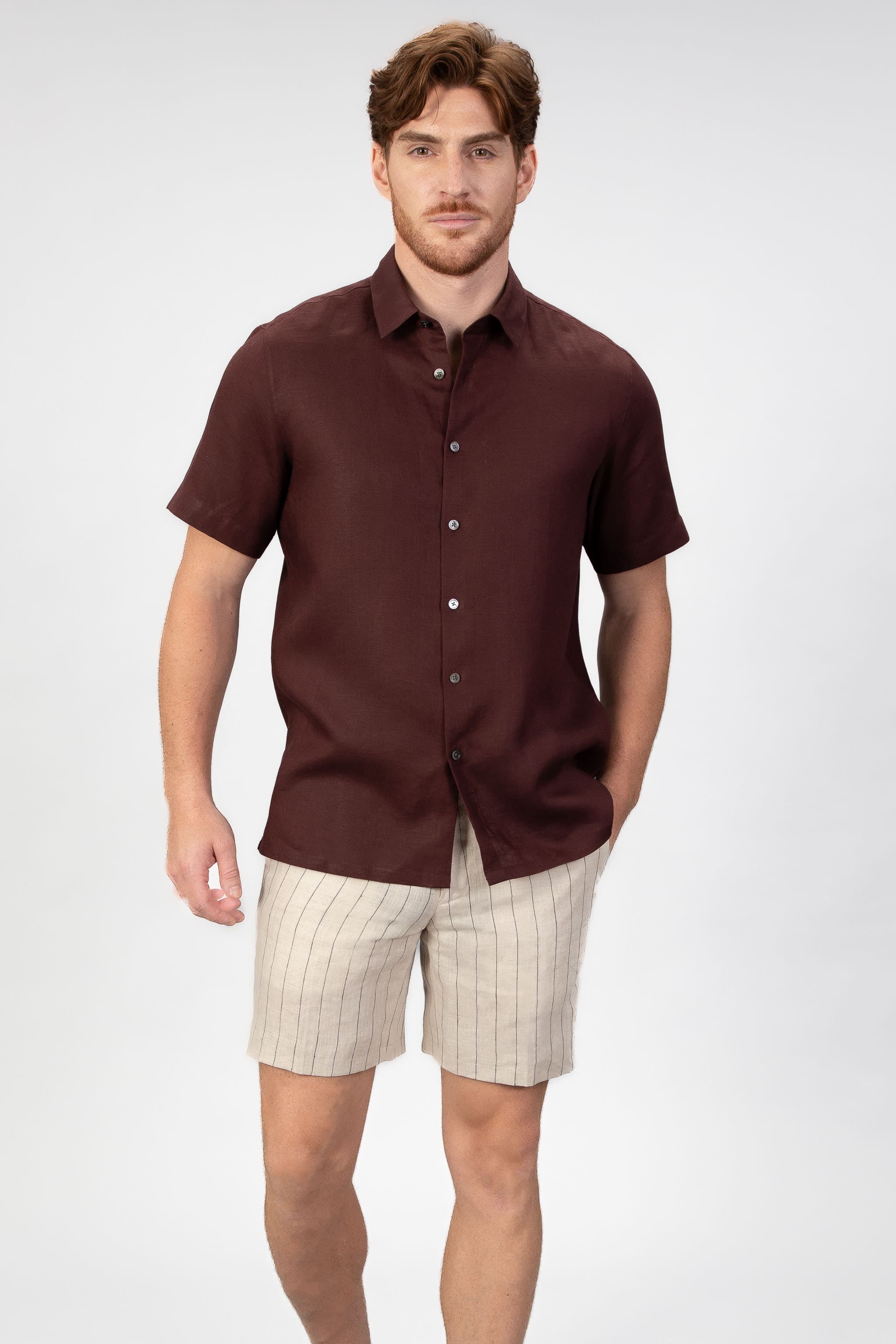 Man wearing a burgundy short-sleeve shirt and beige shorts on a white background