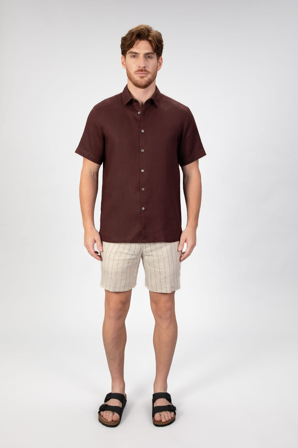 Person wearing a burgundy red short sleeve linen shirt with beige striped linen shorts on light gray background