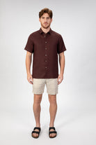 Person wearing a burgundy red short sleeve linen shirt with beige striped linen shorts on light gray background