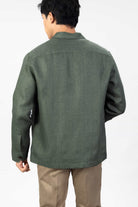 Man wearing a green linen overshirt with beige chinos on a light gray background