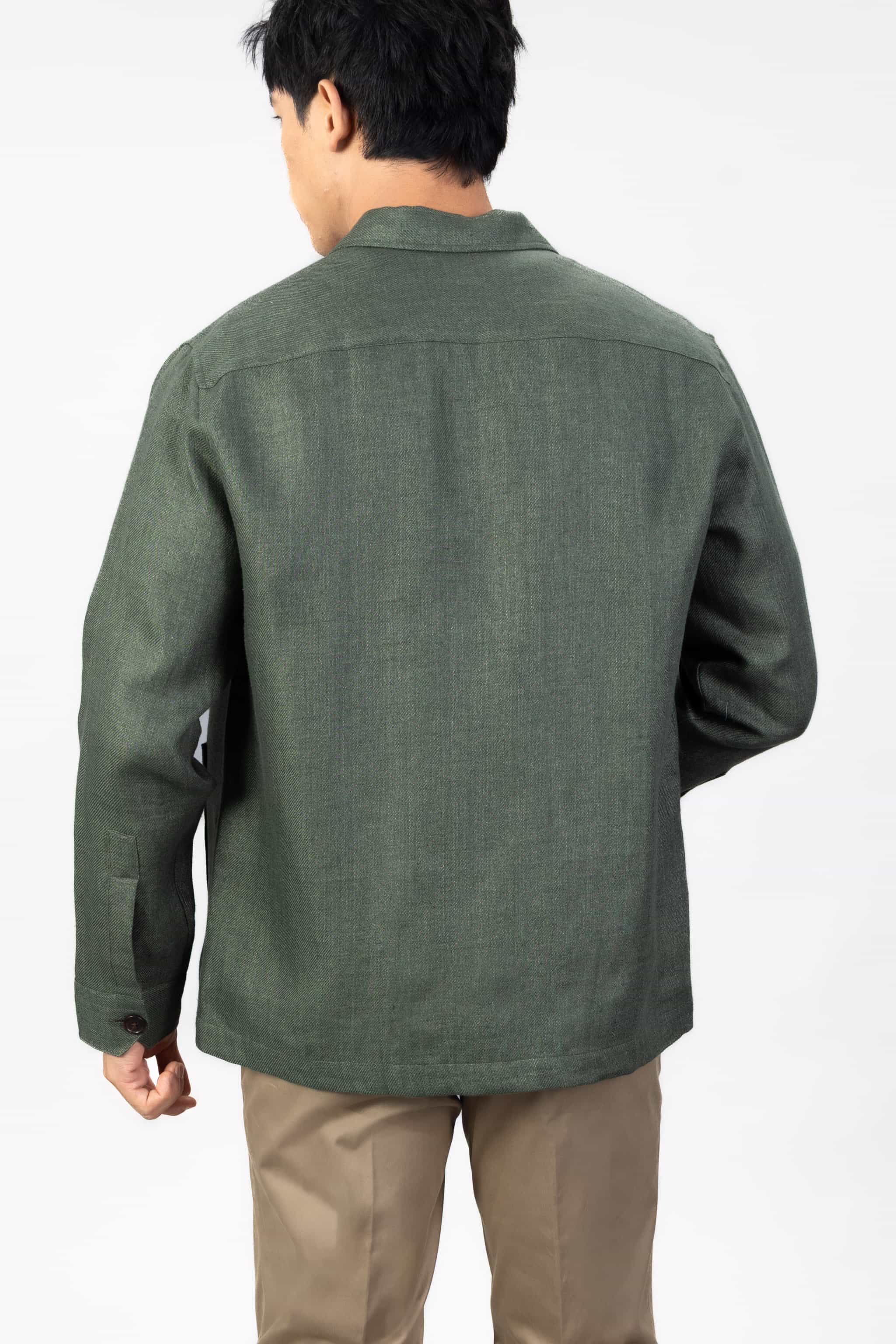 Man wearing a green linen overshirt with beige chinos on a light gray background