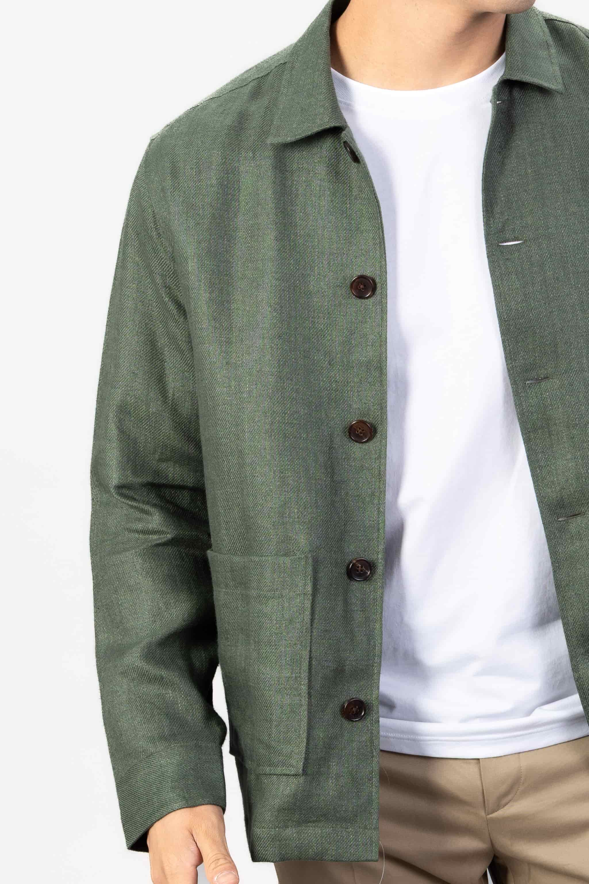 Person wearing a green linen overshirt over a white T-shirt with beige chinos on a light gray background