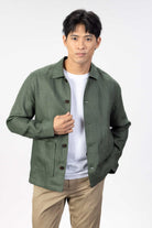 Person wearing a green linen overshirt over a white T-shirt with beige chinos on a light gray background