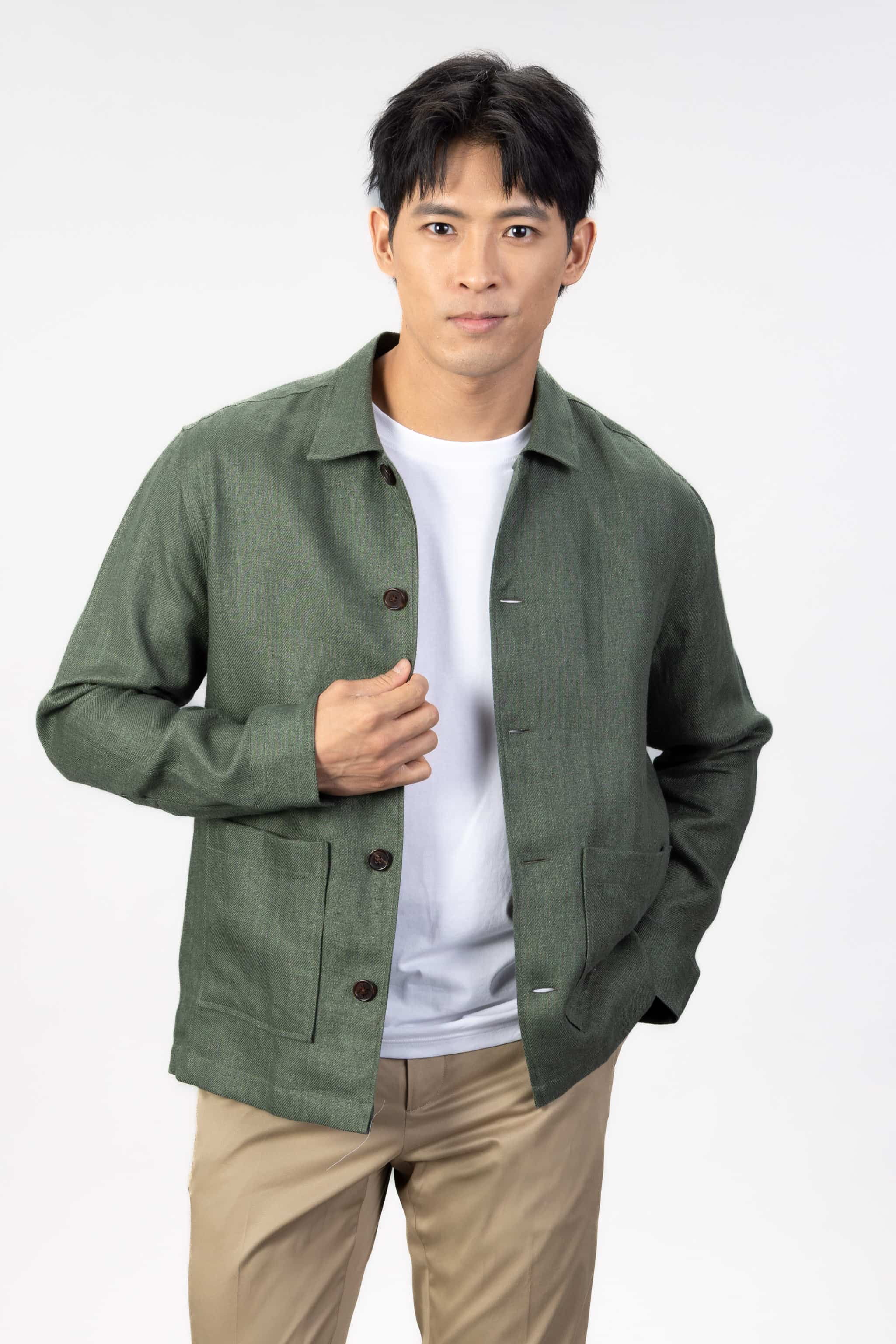 Person wearing a green linen overshirt over a white T-shirt with beige chinos on a light gray background