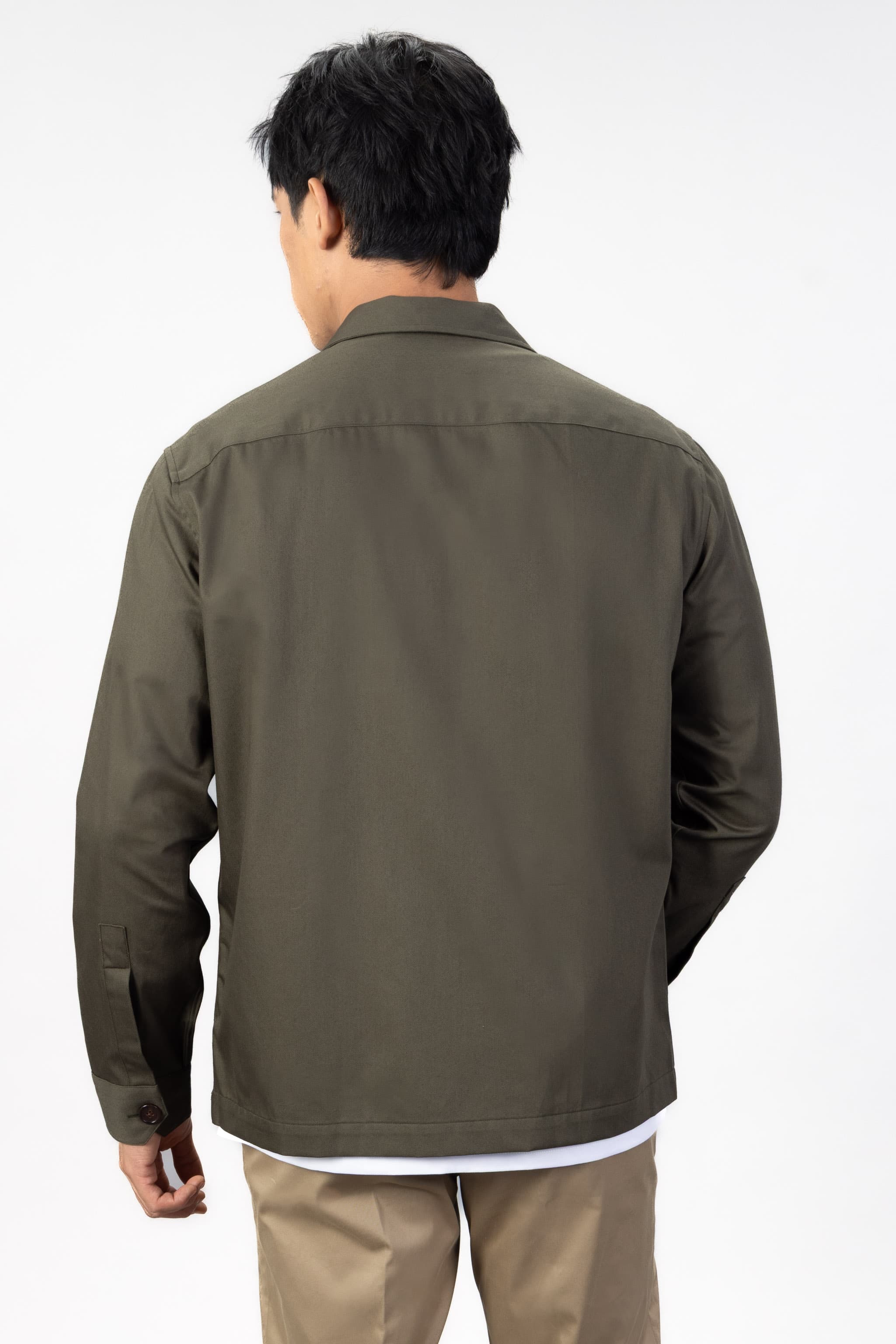 Person wearing a green over shirt over a white T-shirt with beige chinos on a light gray background