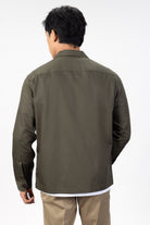 Person wearing a green over shirt over a white T-shirt with beige chinos on a light gray background