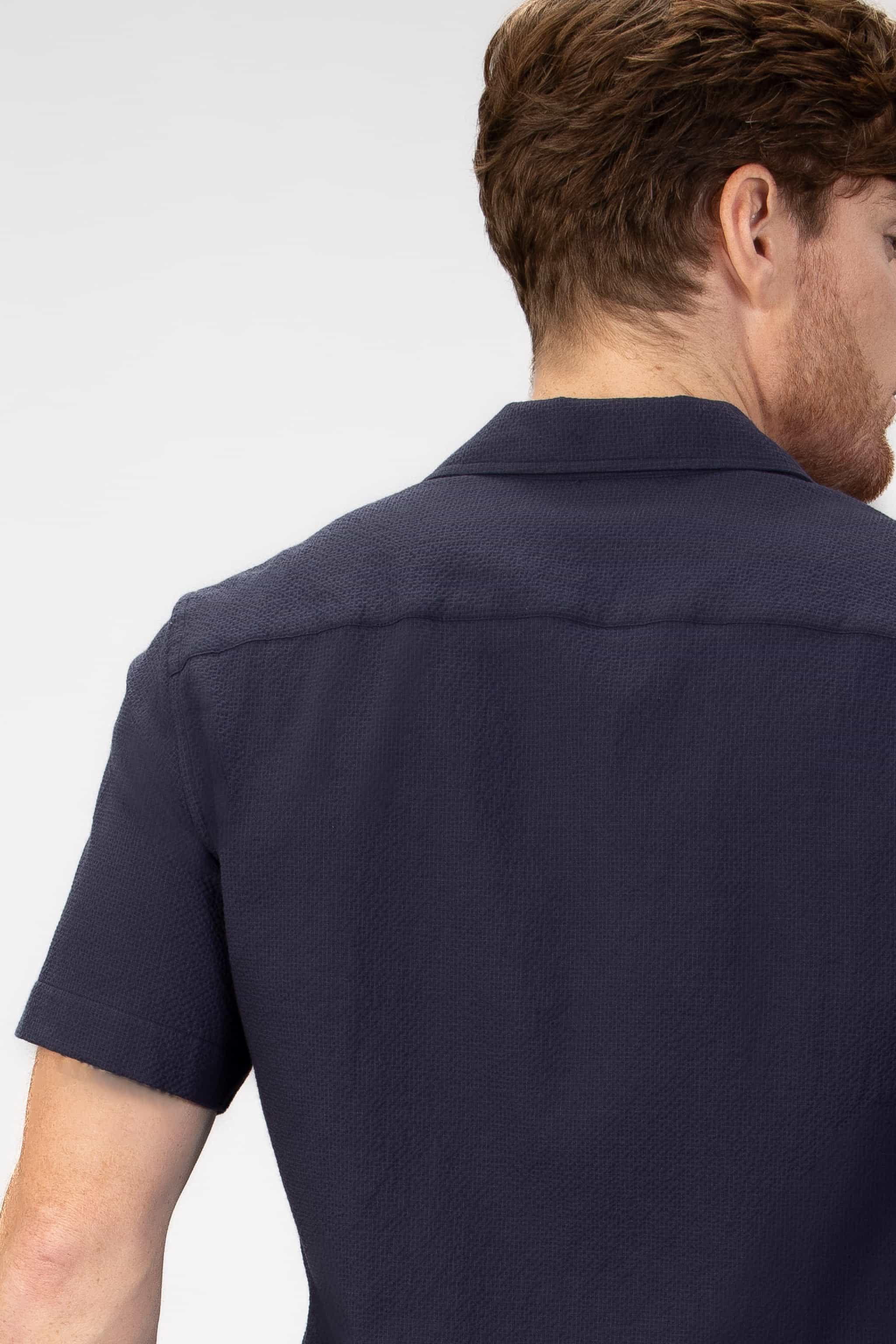 Man wearing a navy camp collar shirt on a light gray background