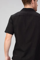 Man wearing a black short-sleeve shirt against a gray background