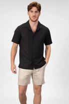 Man wearing a black short-sleeve shirt and beige shorts on a white background