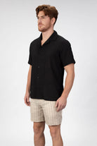 Man wearing a short sleeve camp collar shirt in black seersucker fabric with matching striped linen shorts in beige.