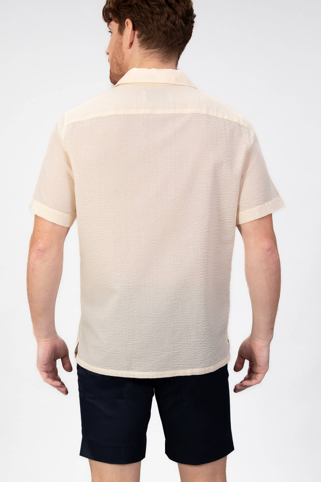 Man wearing a beige-yellow seersucker camp collar shirt  on light gray background