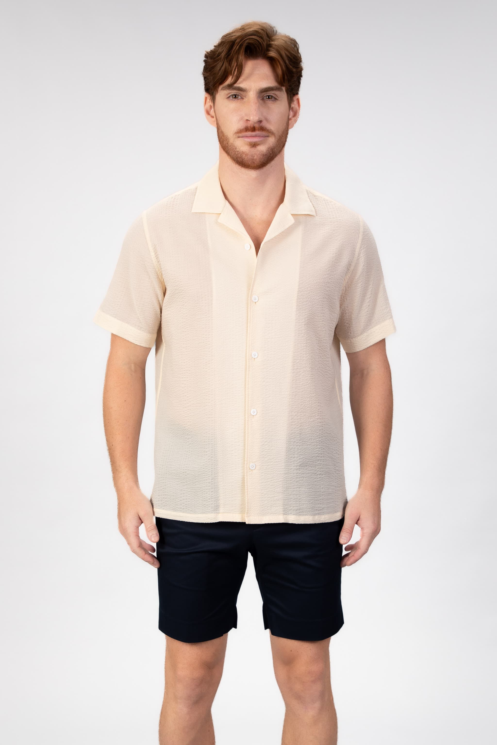 Man wearing a beige-sand seersucker camp collar shirt  on light gray background