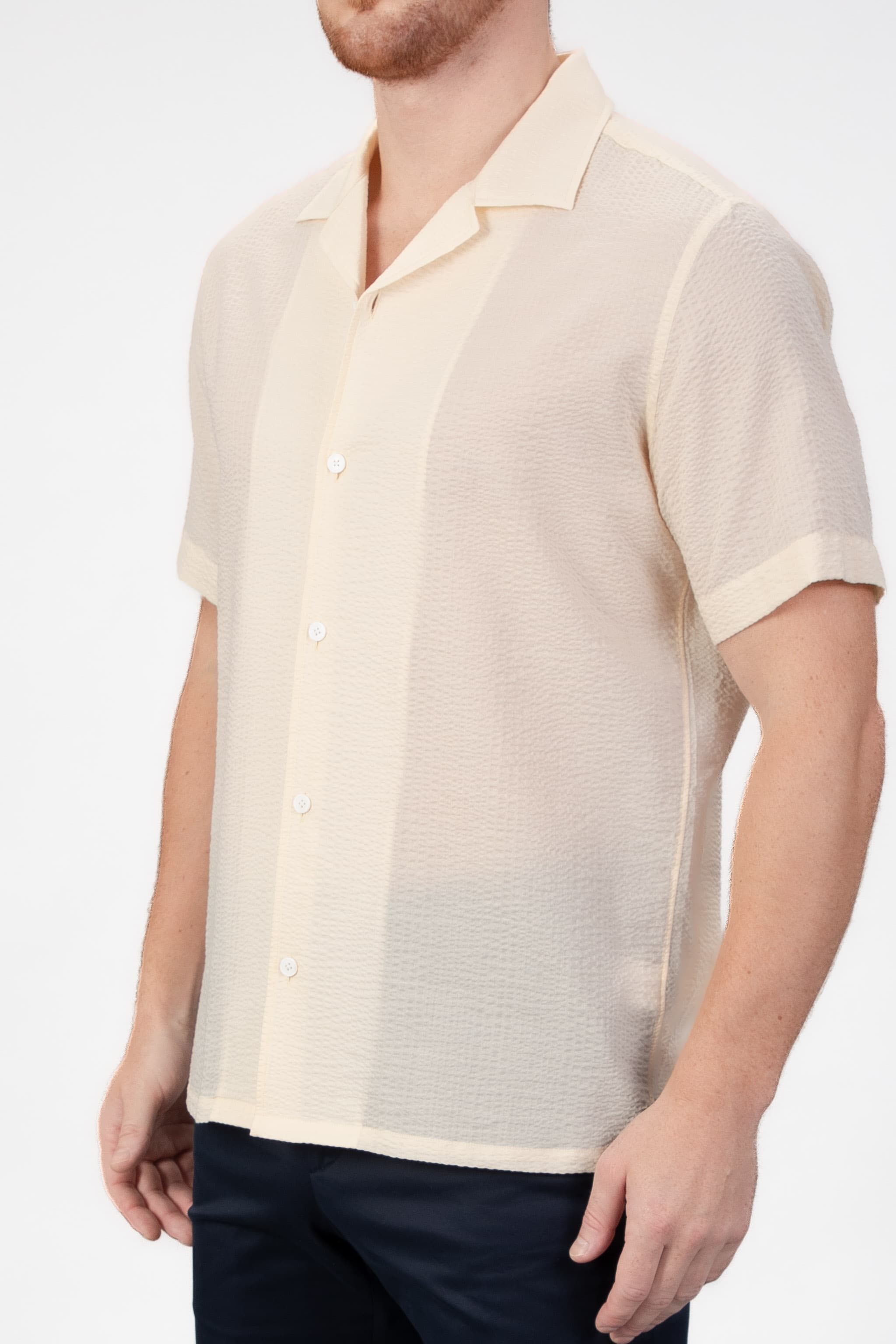 Man wearing a beige-sand seersucker camp collar shirt  on light gray background