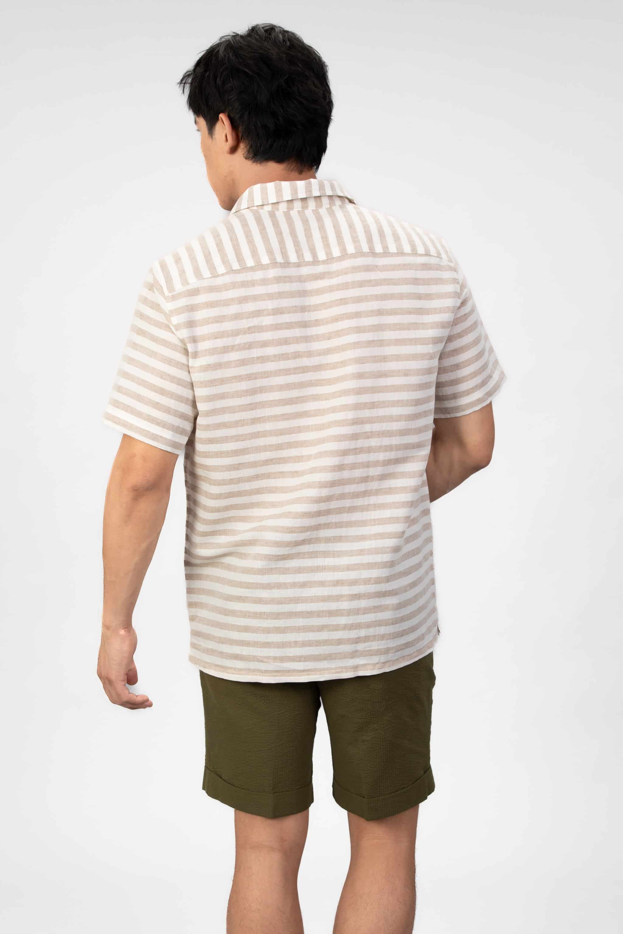 Man wearing a striped linen shirt and green shorts on a light gray background