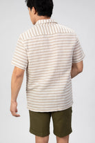 Man wearing a striped shirt and green shorts against a gray background