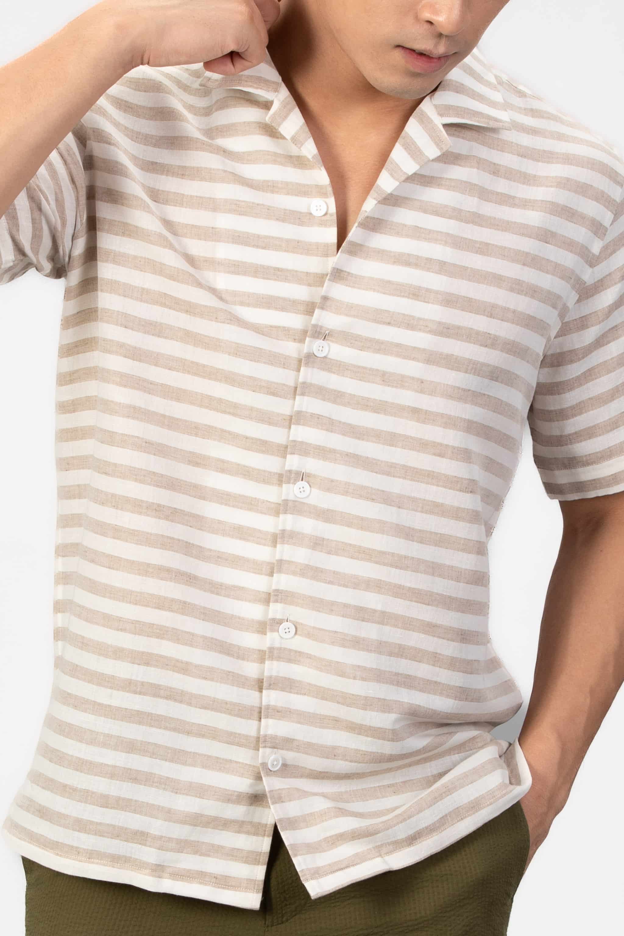 Man wearing a striped linen shirt and green shorts on a light gray background
