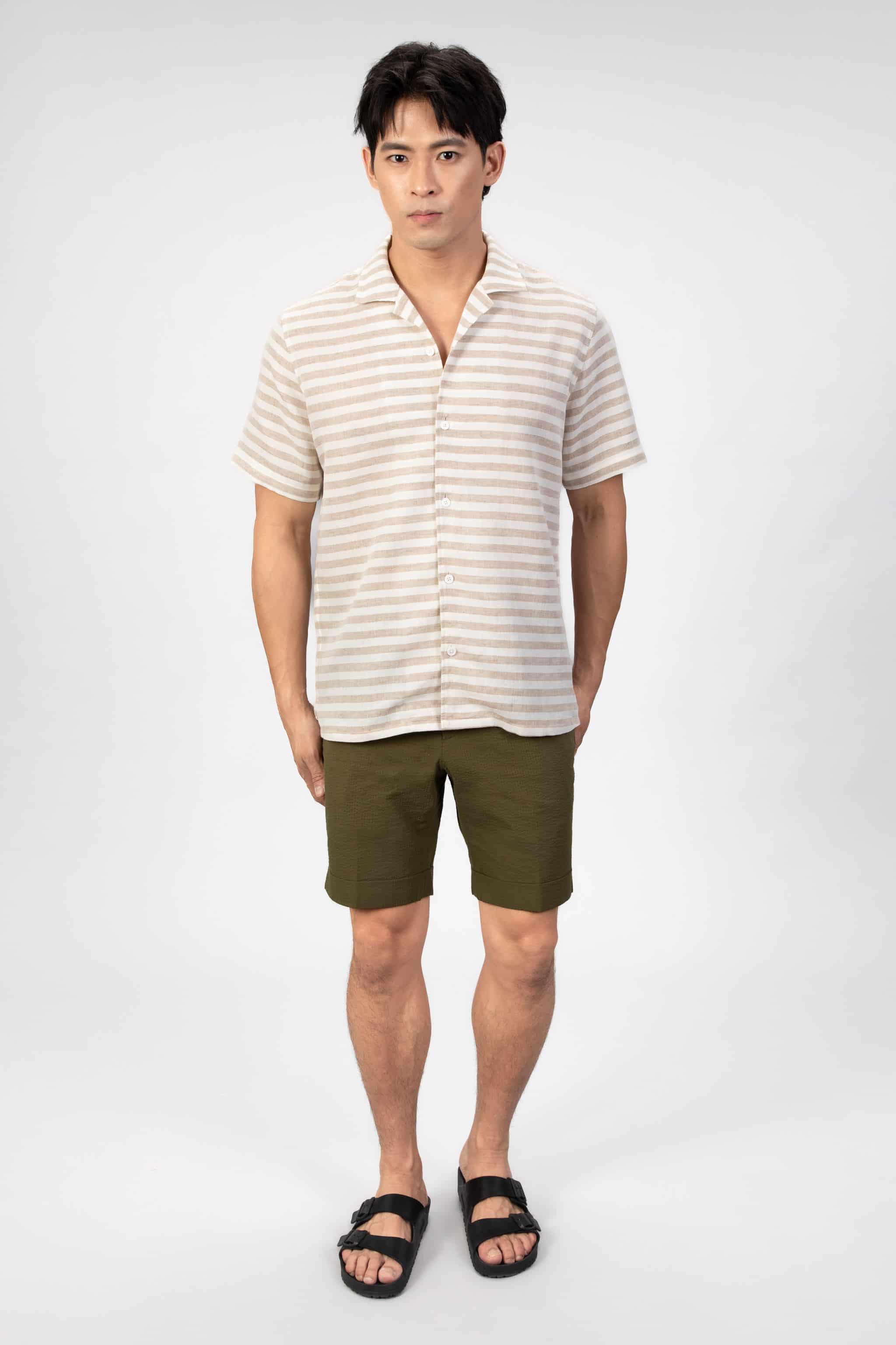 Man wearing a striped linen shirt and green shorts on a light gray background