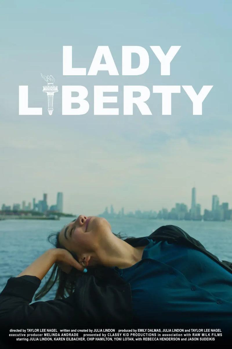 Movie poster for 'Lady Liberty' featuring a woman reclining by the water with a city skyline in the background, under a pale blue sky with large white title text.