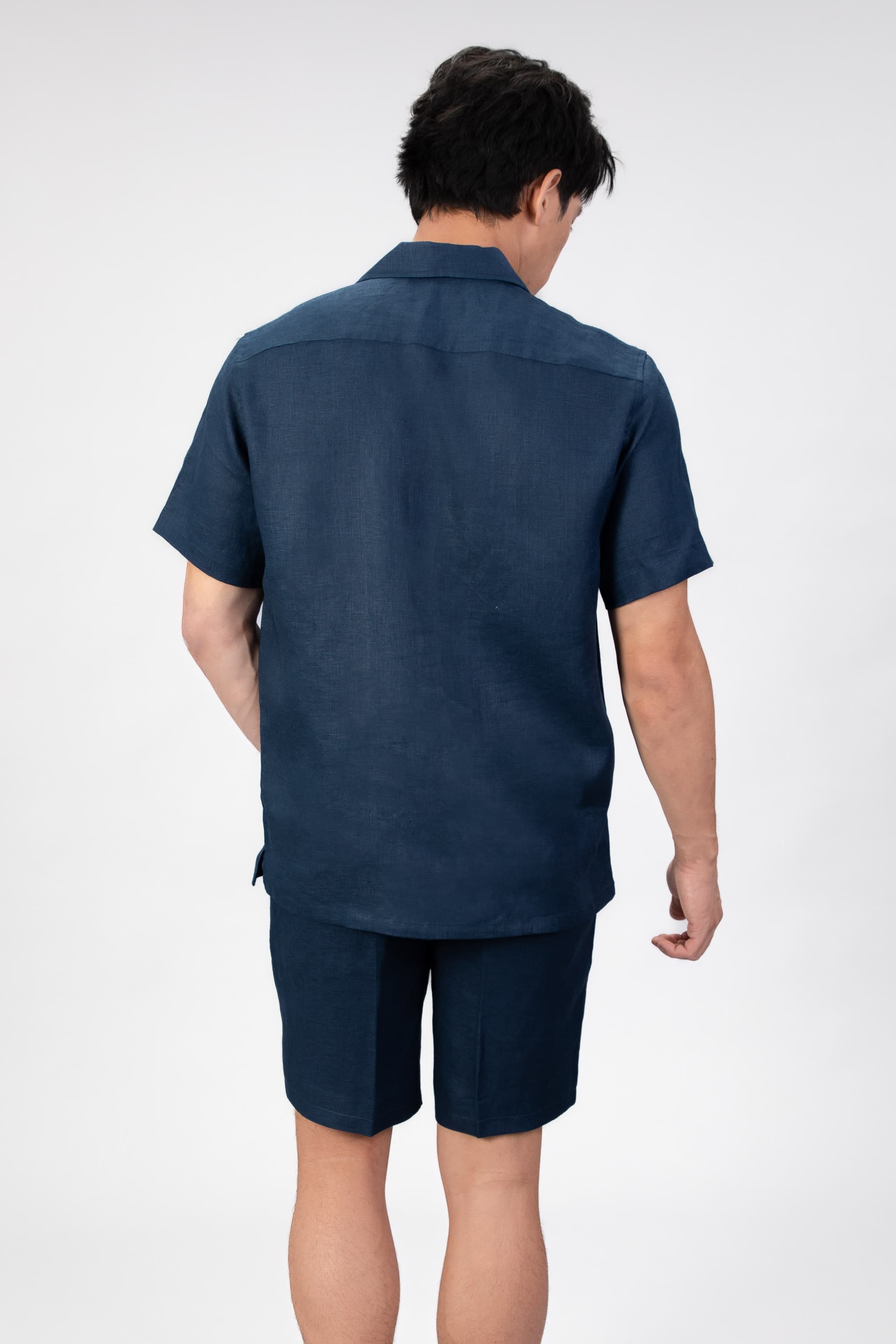 Person wearing navy blue linen set, camp collar shirt and shorts on light gray background