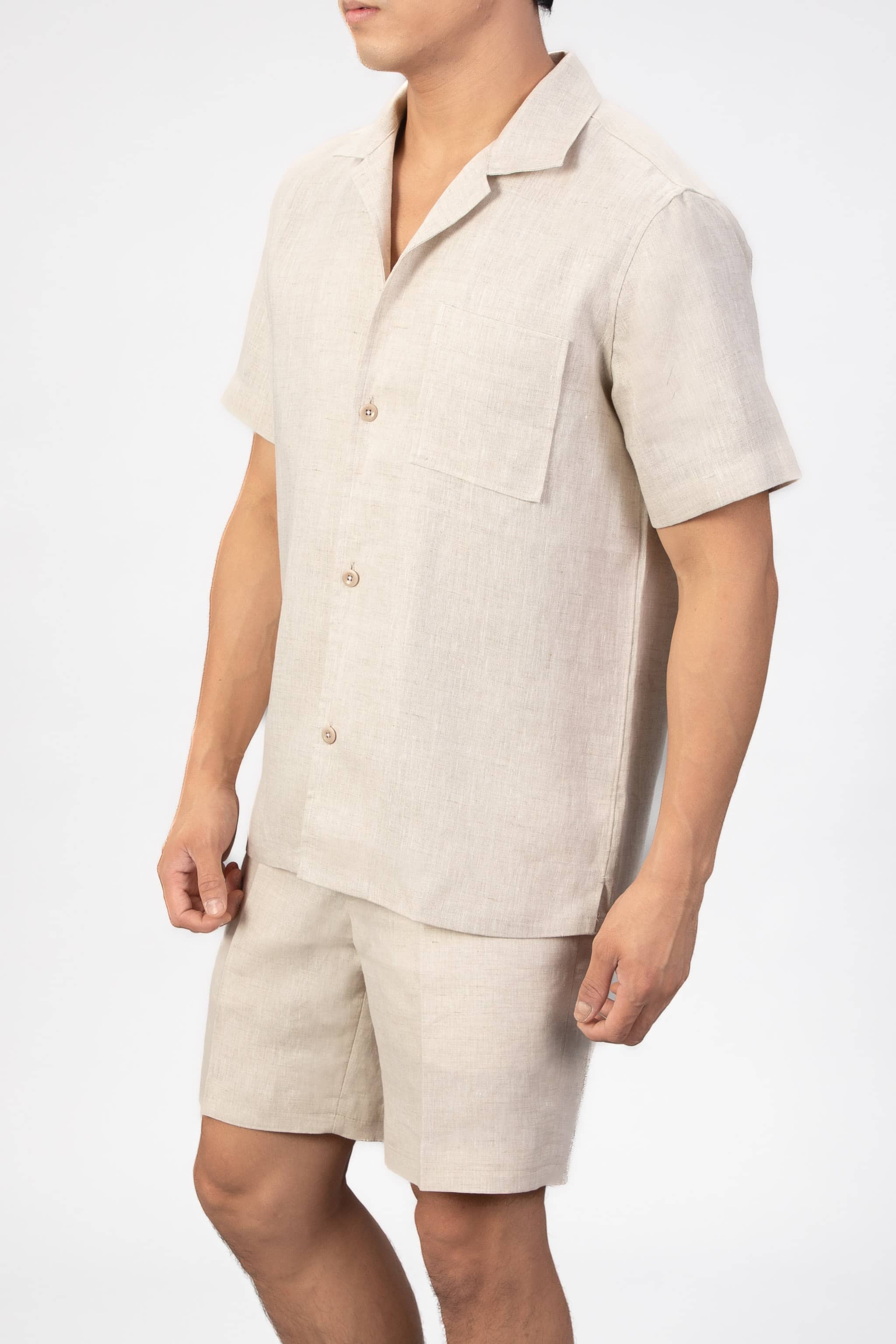 Person wearing a beige linen shirt and shorts set on a white background