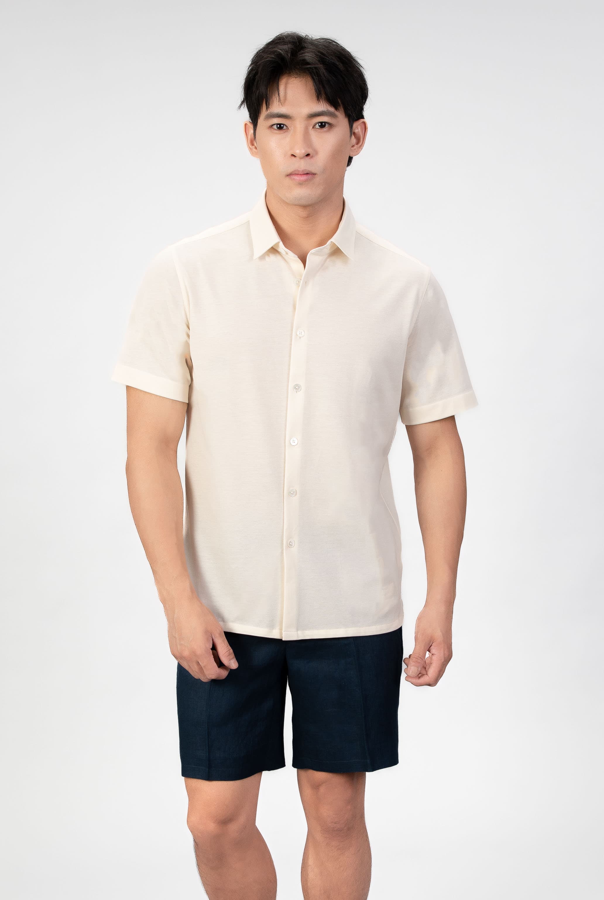 Man wearing a sand-beige piquet polo shirt sleeve shirt with linen navy shorts on a light gray background