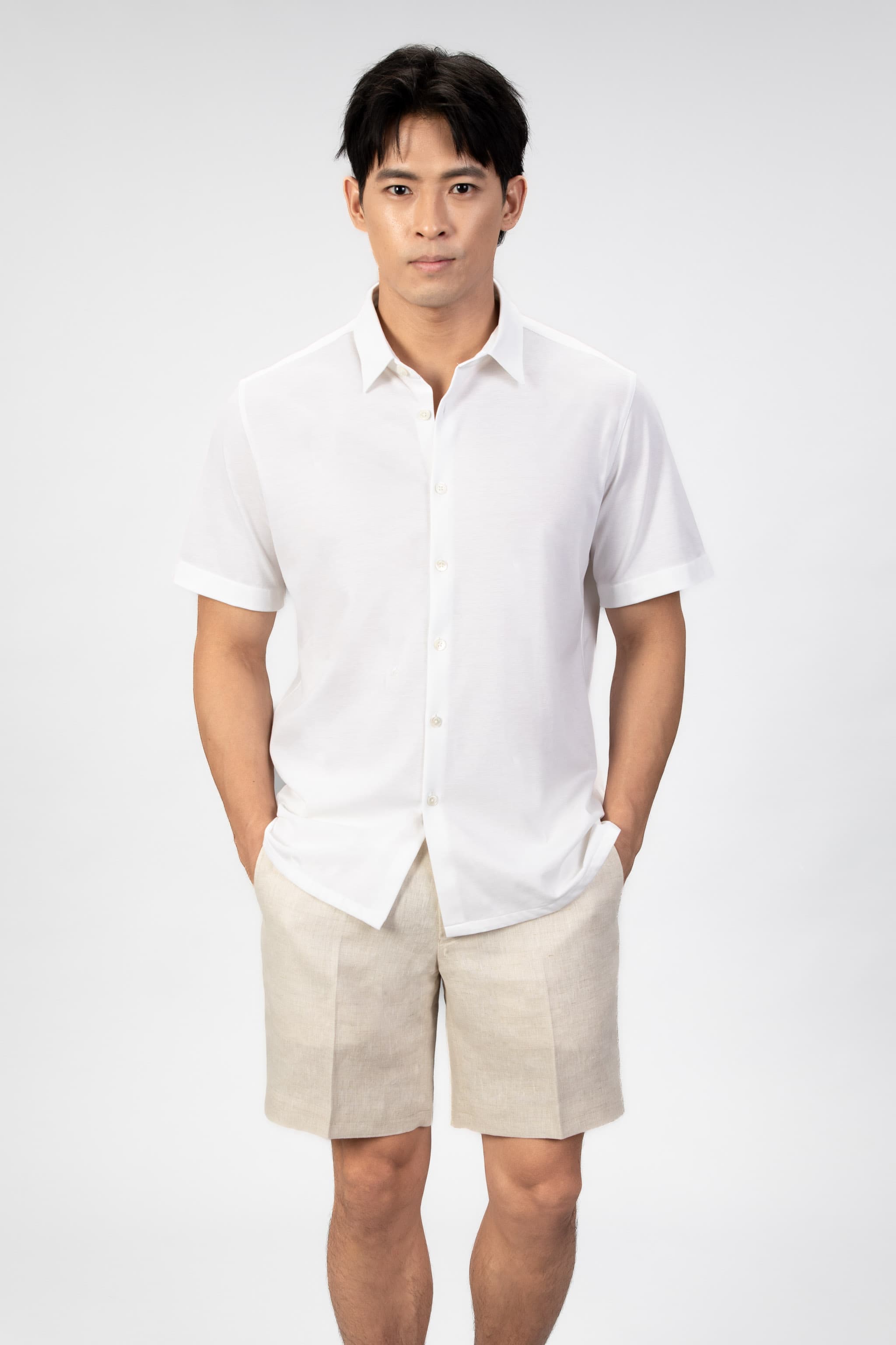 Man wearing a white short-sleeve shirt and beige shorts on a light gray background