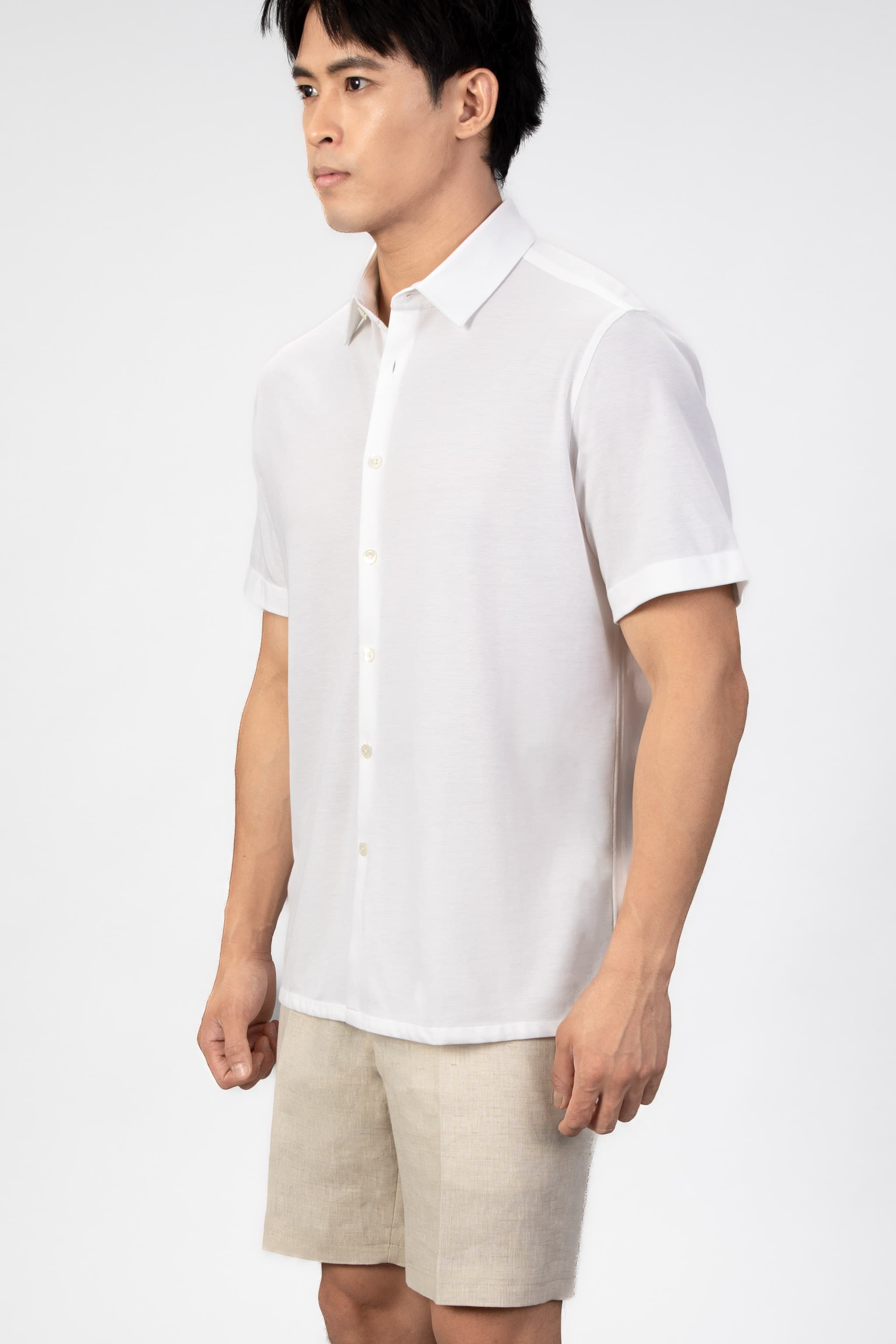 Man wearing a white short-sleeve shirt and beige shorts on a plain background