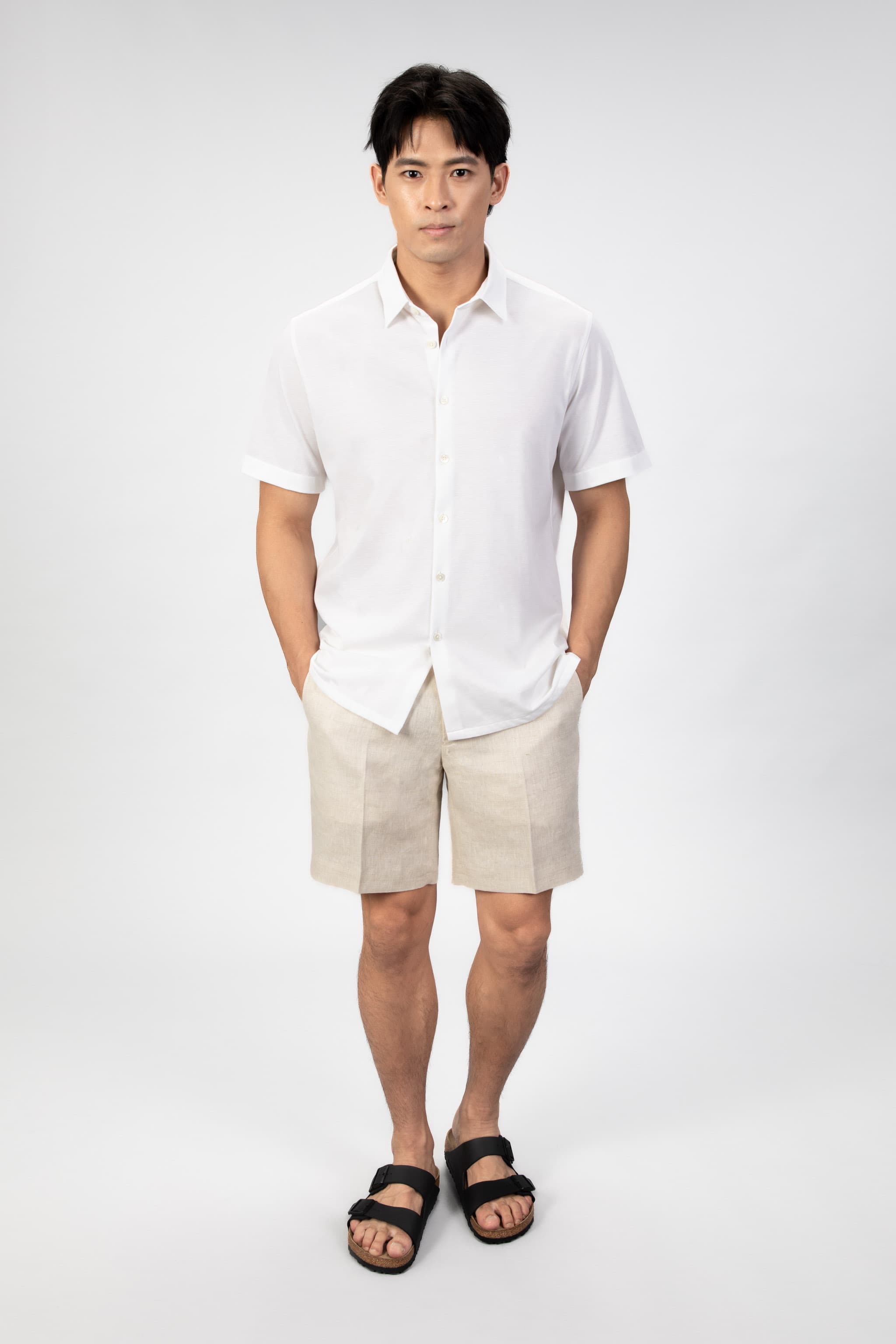 Man wearing a white piquet polo shirt and beige linen shorts on a light gray background